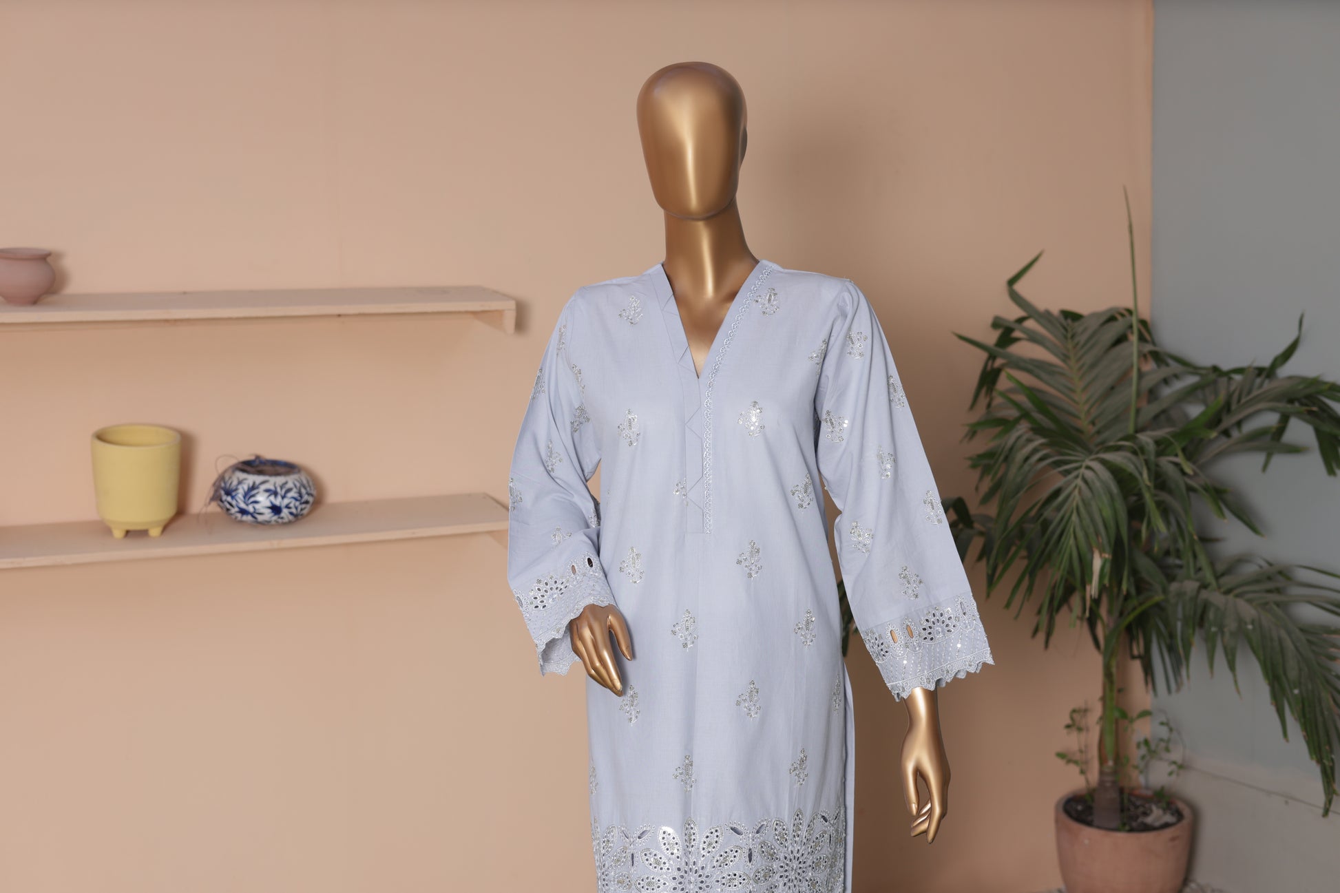 Mannequin wearing a light blue dress with lace details against a beige wall.