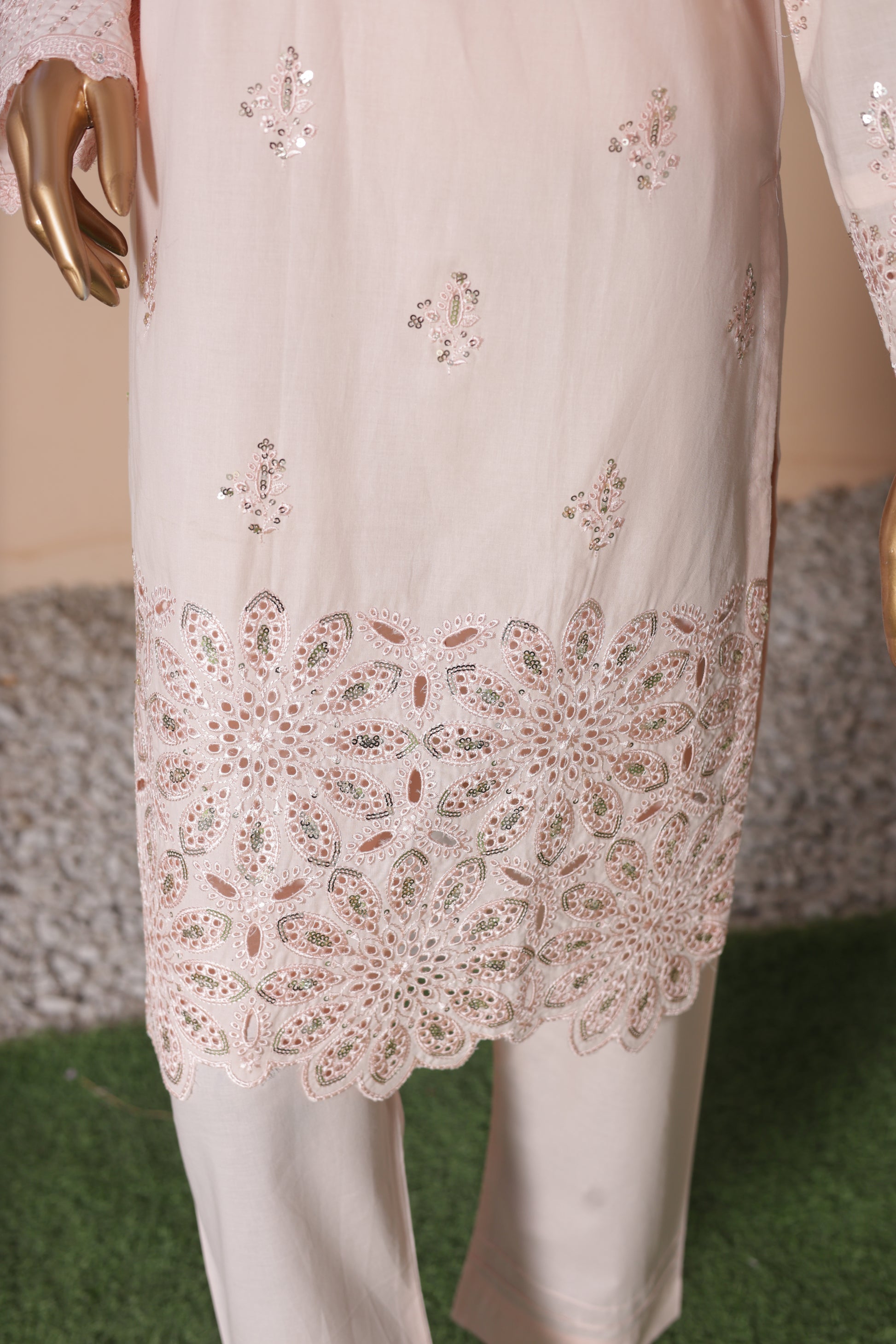 White embroidered outfit with a gold hand holding it, on a blurred background.