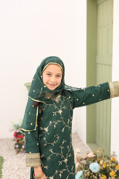 Child wearing a green traditional outfit with gold embroidery indoors.