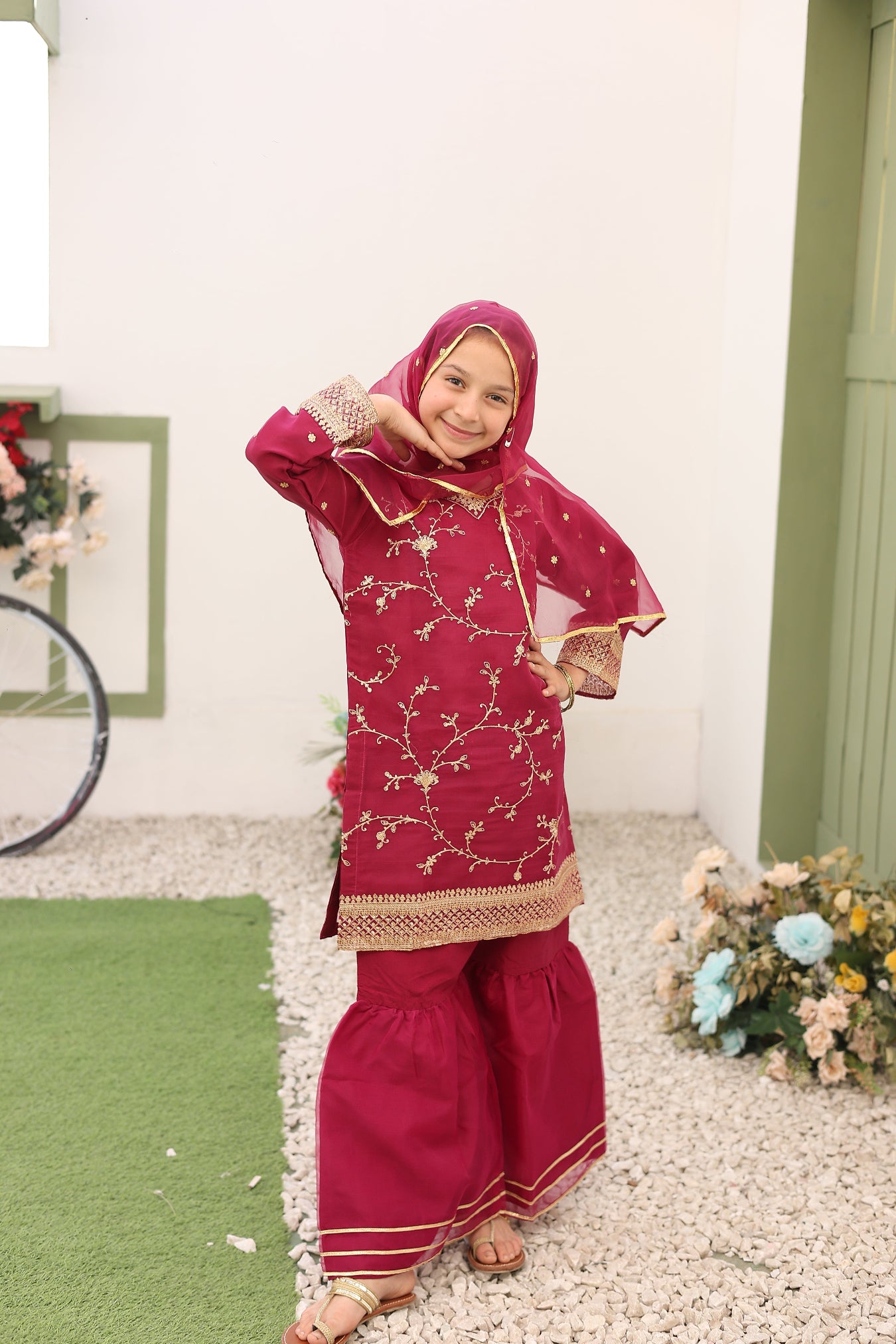Child in a red traditional outfit with gold patterns on a white floor.