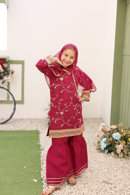 Child in a red traditional outfit with gold patterns on a white floor.