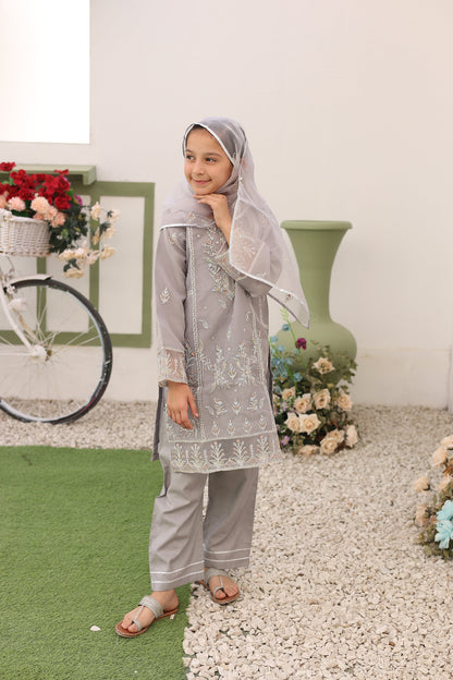 Woman in a gray traditional outfit standing on a checkered floor with flowers around her.