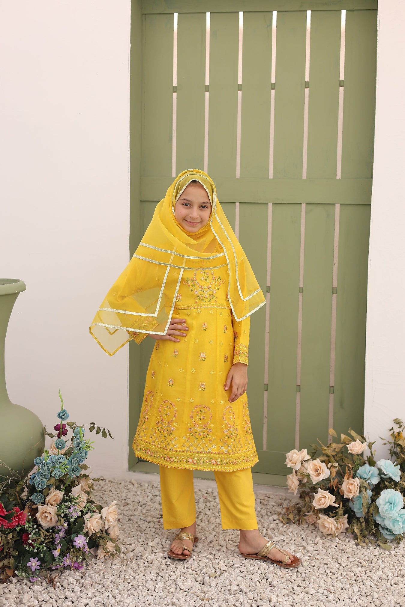 Woman in a yellow traditional outfit standing in front of a green door with floral decorations.
