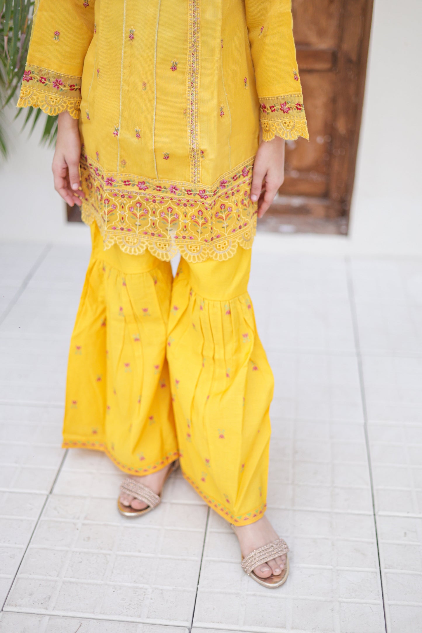 Person wearing a yellow traditional outfit with intricate patterns on a white floor.