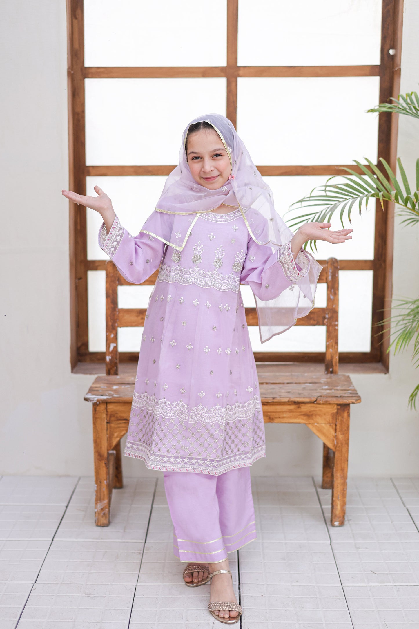 Woman in a light purple traditional outfit standing in front of a wooden window frame.