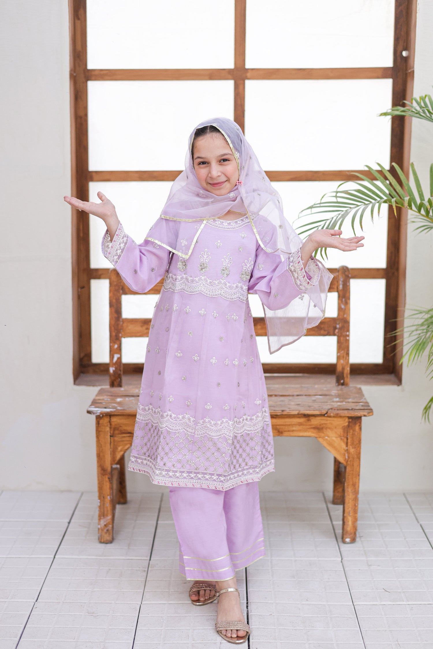 Woman in a light purple traditional outfit standing in front of a wooden window frame.