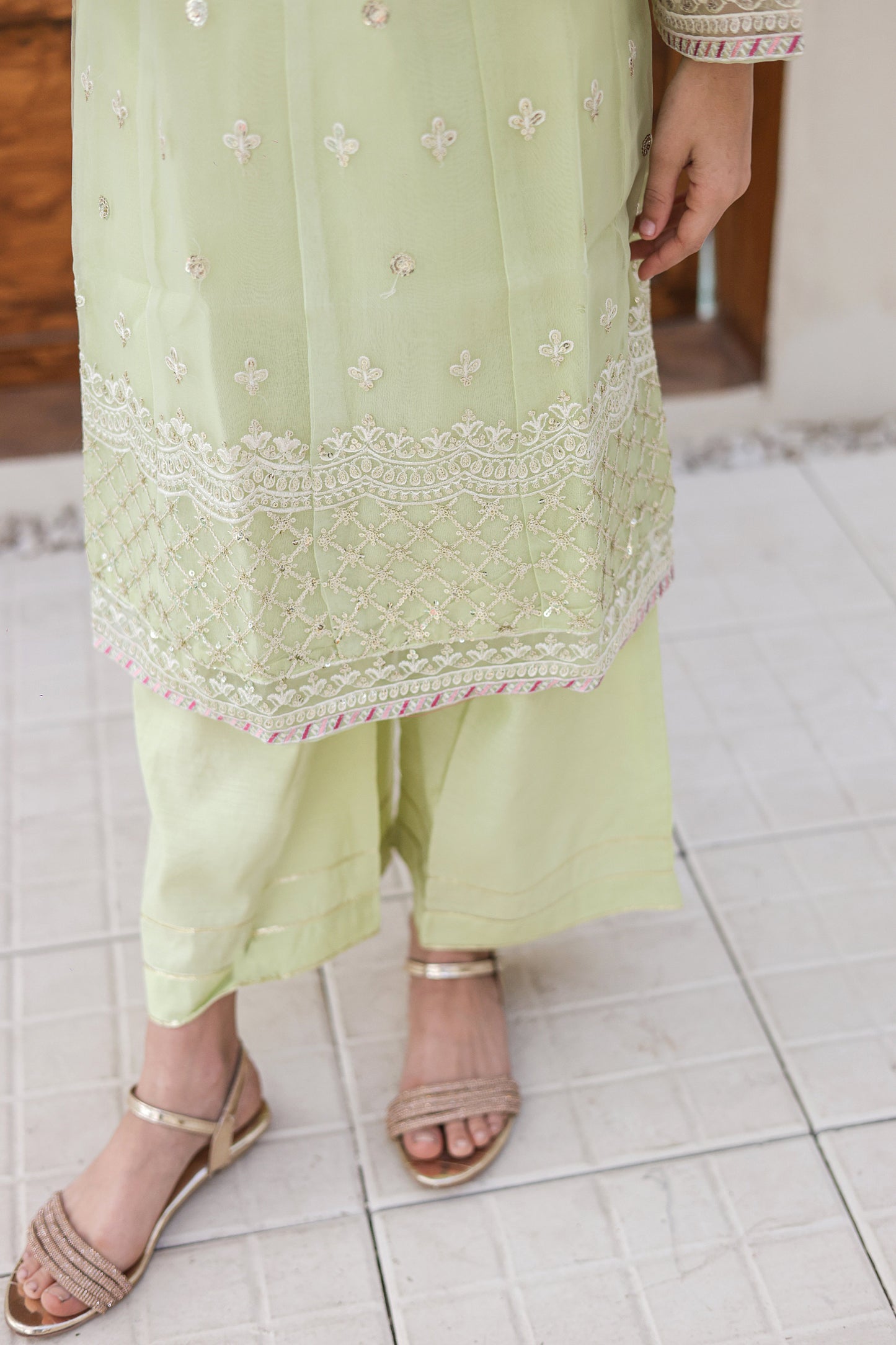 Light green traditional outfit with intricate embroidery on a tiled floor.