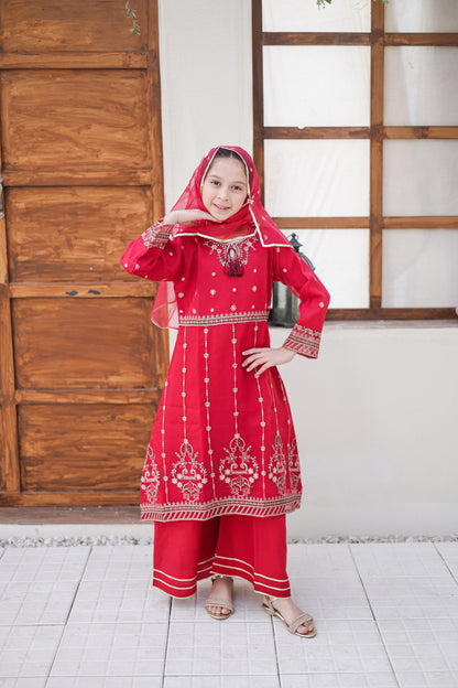 Person wearing a red traditional outfit with white patterns in a room with wooden doors and a white wall.