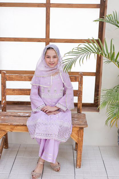 Woman in a light purple traditional outfit sitting on a wooden bench with a plant in the background.