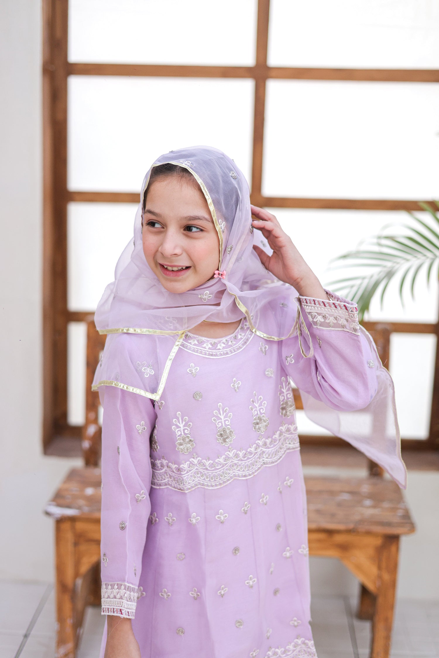 Young girl wearing a light purple traditional outfit with a matching headscarf indoors.