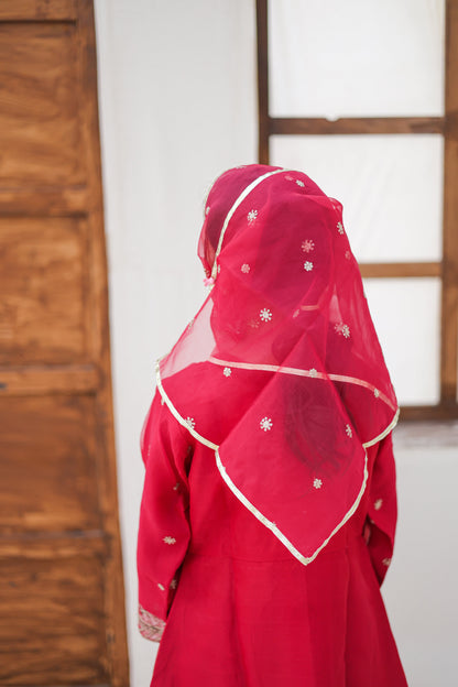 Person wearing a red traditional outfit with a matching headscarf in a room.
