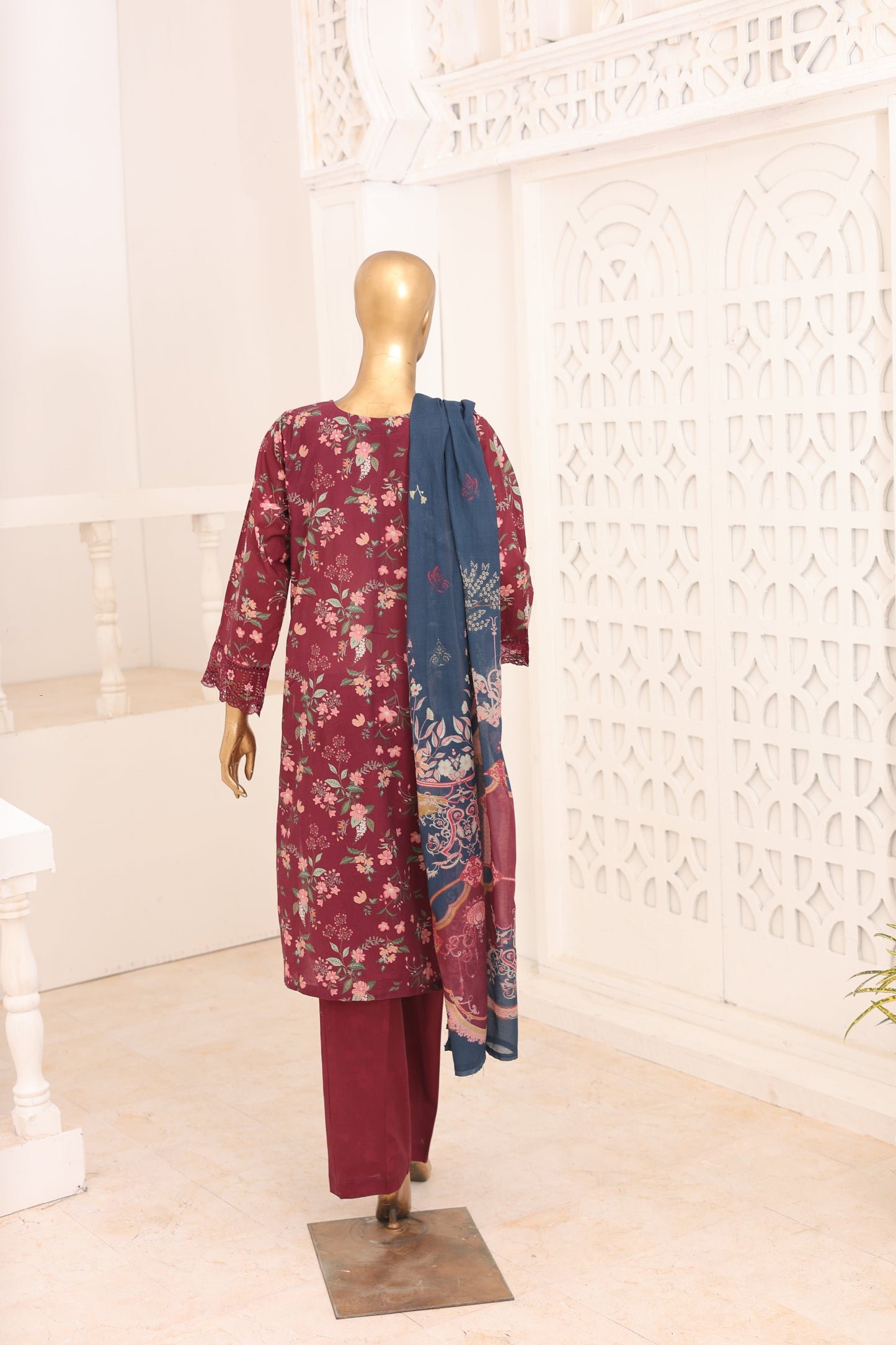 Mannequin wearing a maroon floral outfit with a blue scarf against a decorative white wall.