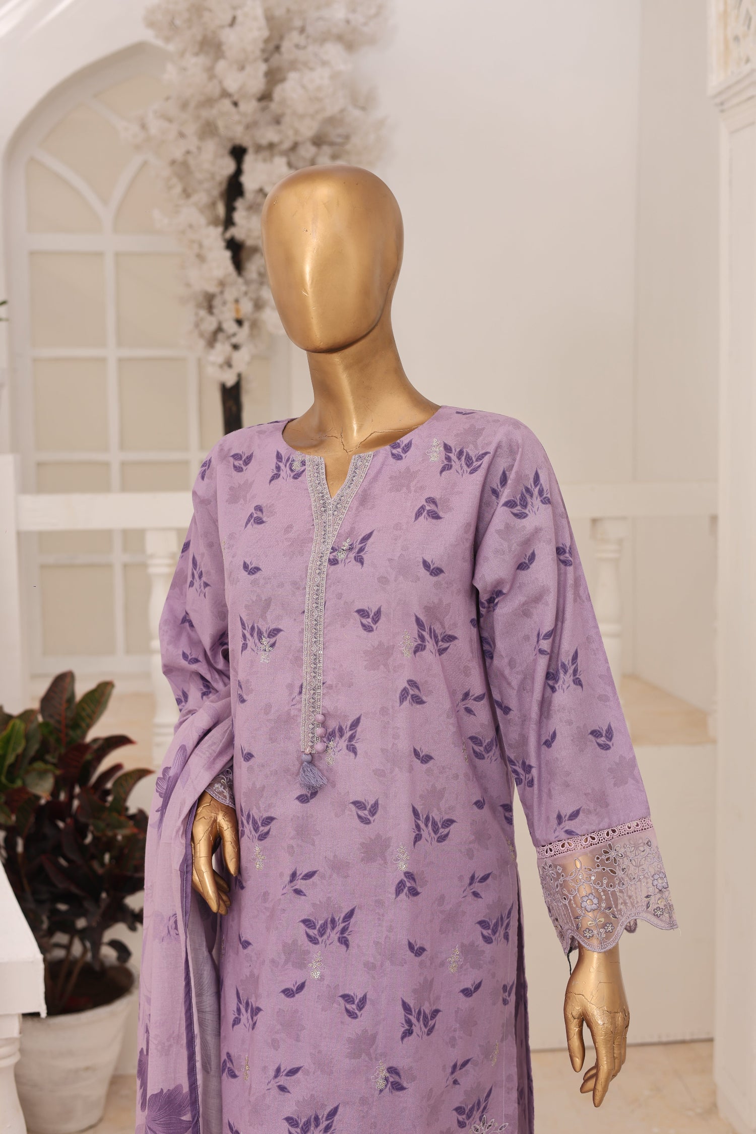 Mannequin wearing a purple dress with floral patterns in a room setting.