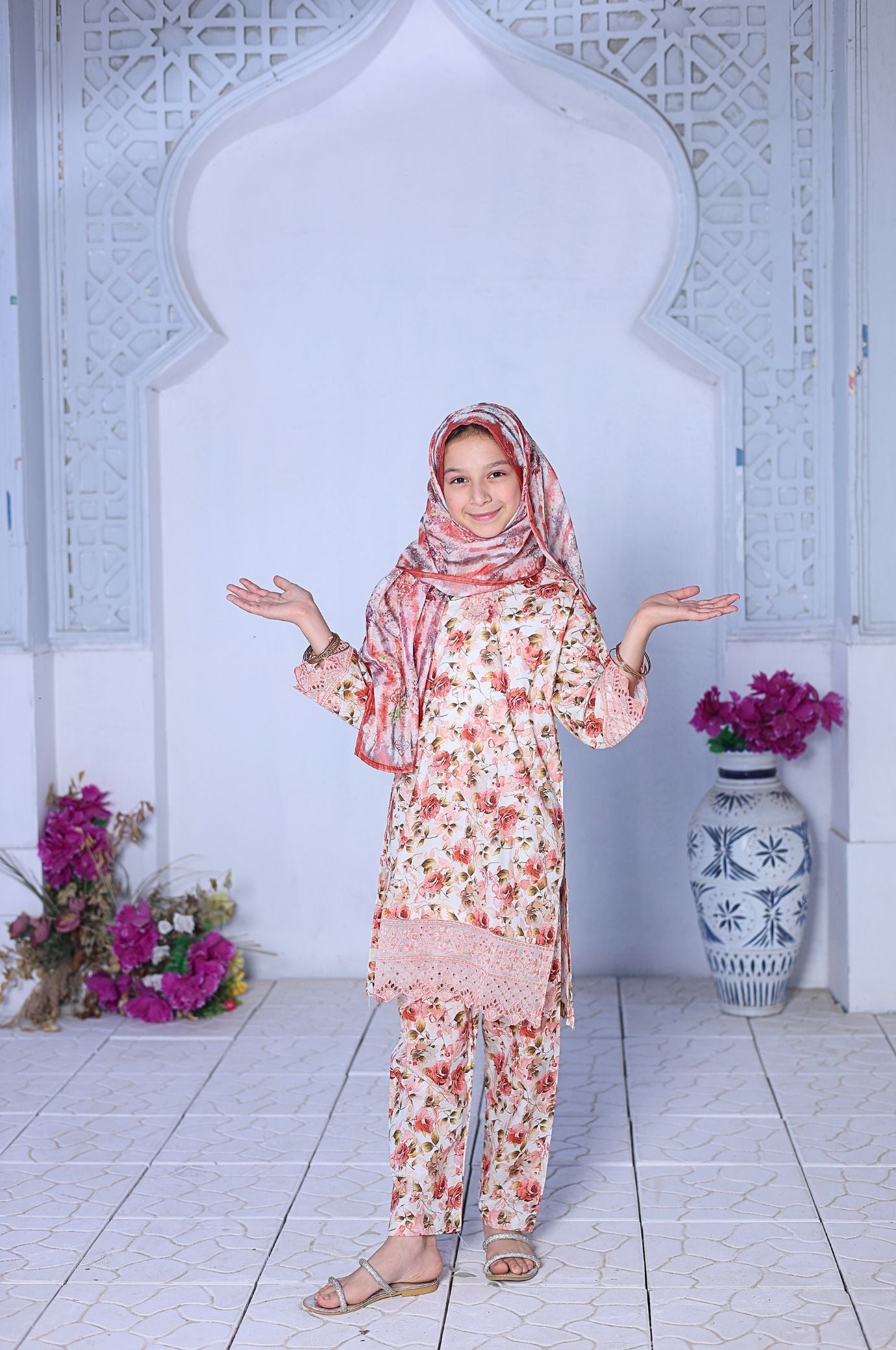 Woman in a floral outfit standing in a decorated room with flowers and a vase.