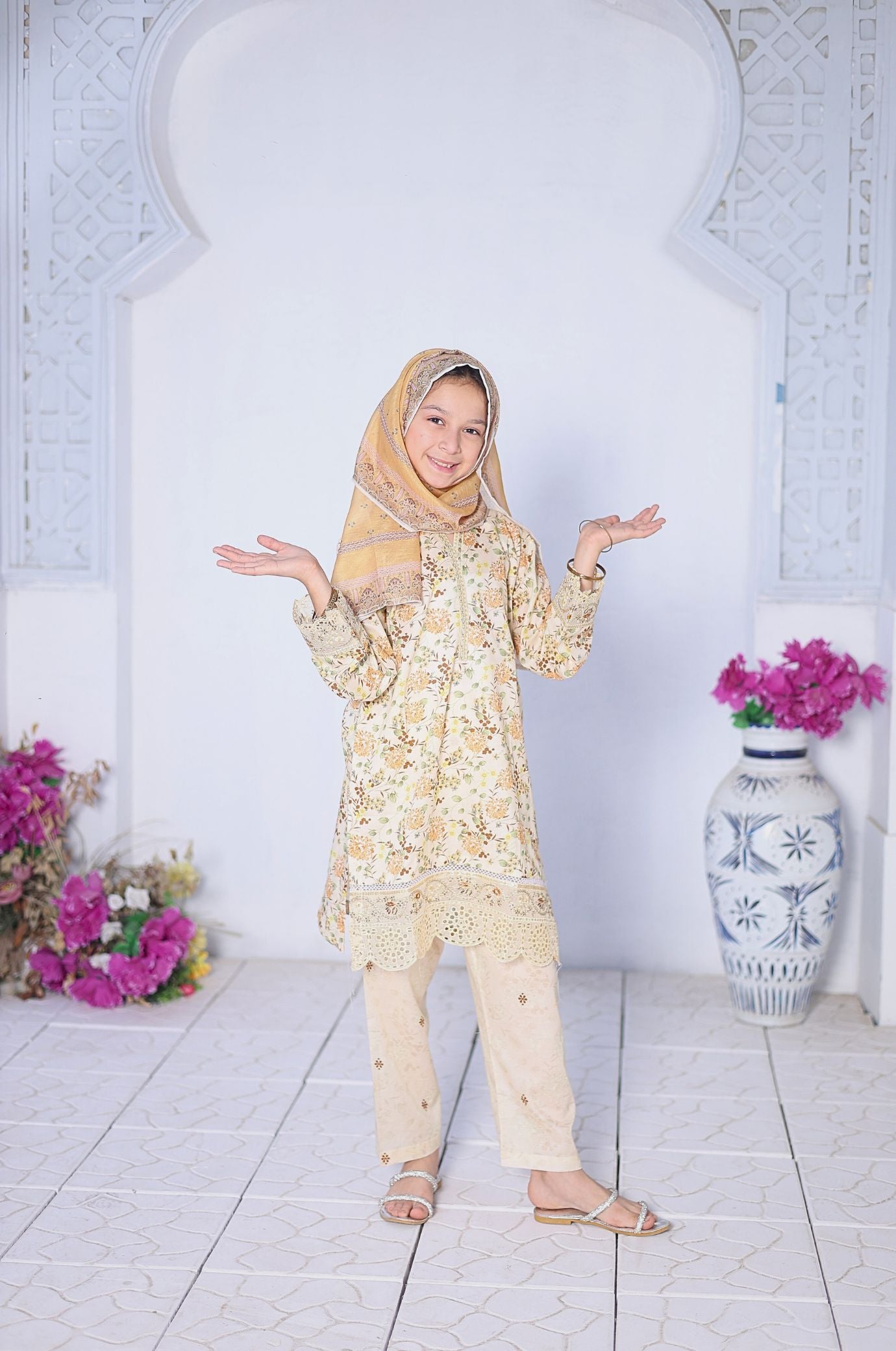Woman in a floral outfit standing in a decorated room with flowers and a vase.
