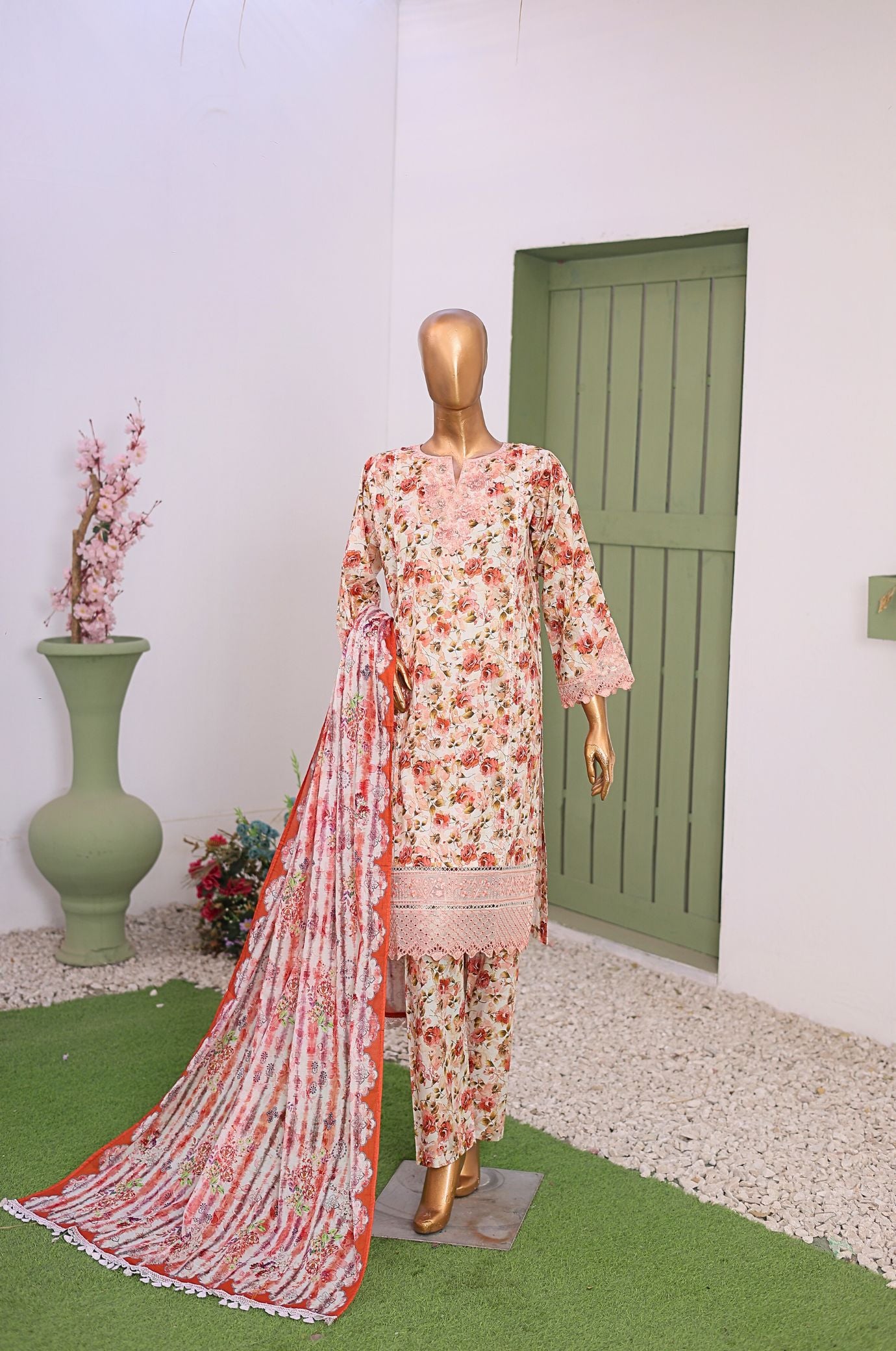 Mannequin wearing a floral dress with a dupatta in a room with a green door and vase.