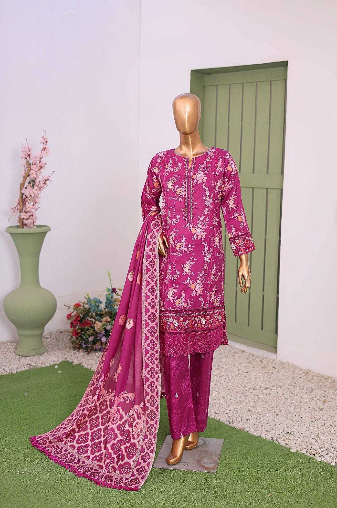 Mannequin wearing a pink embroidered traditional outfit with a matching dupatta in a room with a green door and decorative items.