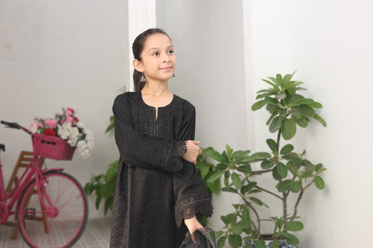 Young girl in a black dress standing indoors with plants and a pink bicycle in the background