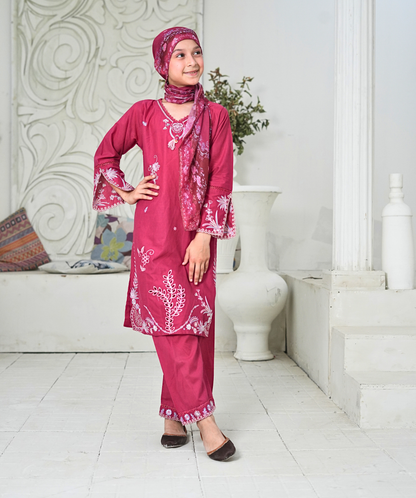 Woman in a pink traditional outfit with matching headscarf standing in a white interior setting.