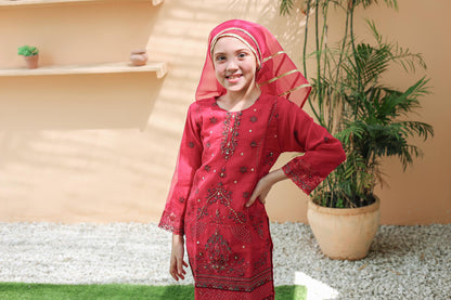 Young girl in a red traditional outfit with a headscarf, standing outdoors.