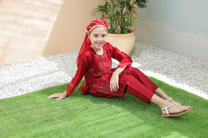 Child in a red outfit sitting on green grass with a plant in the background