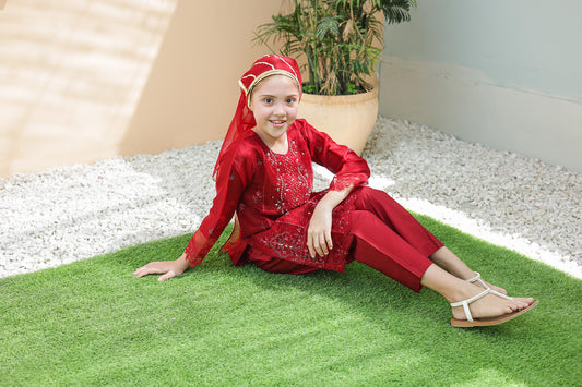 Child in a red outfit sitting on green grass with a plant in the background