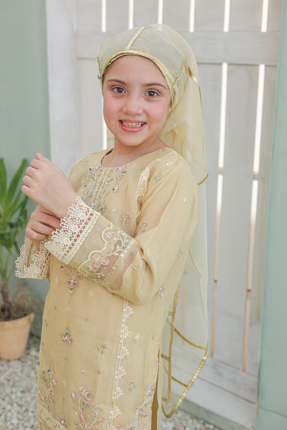 Young girl wearing a beige embroidered dress with a matching headscarf in a light indoor setting.