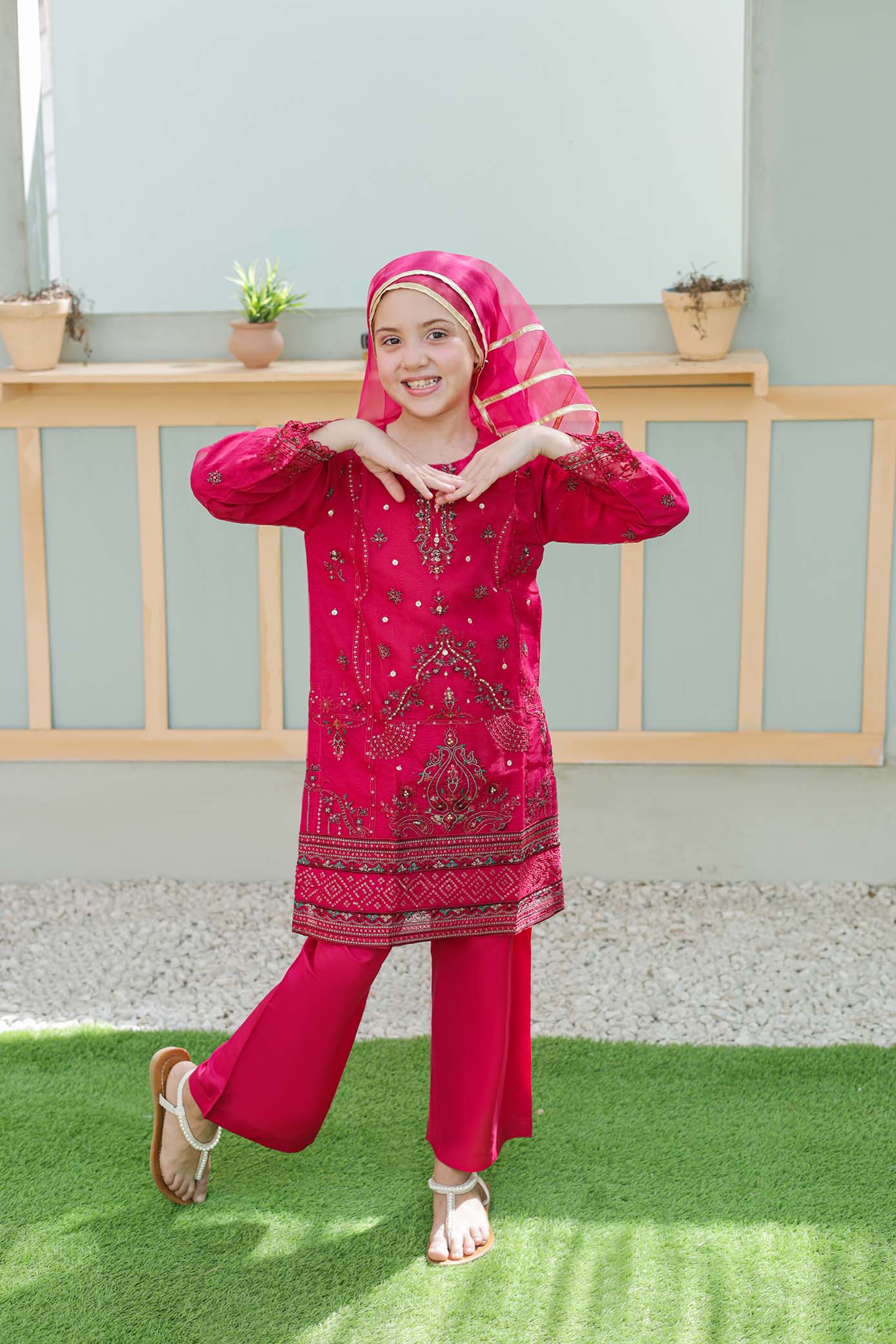 Child wearing a red embroidered outfit with a matching headscarf on a grassy area.