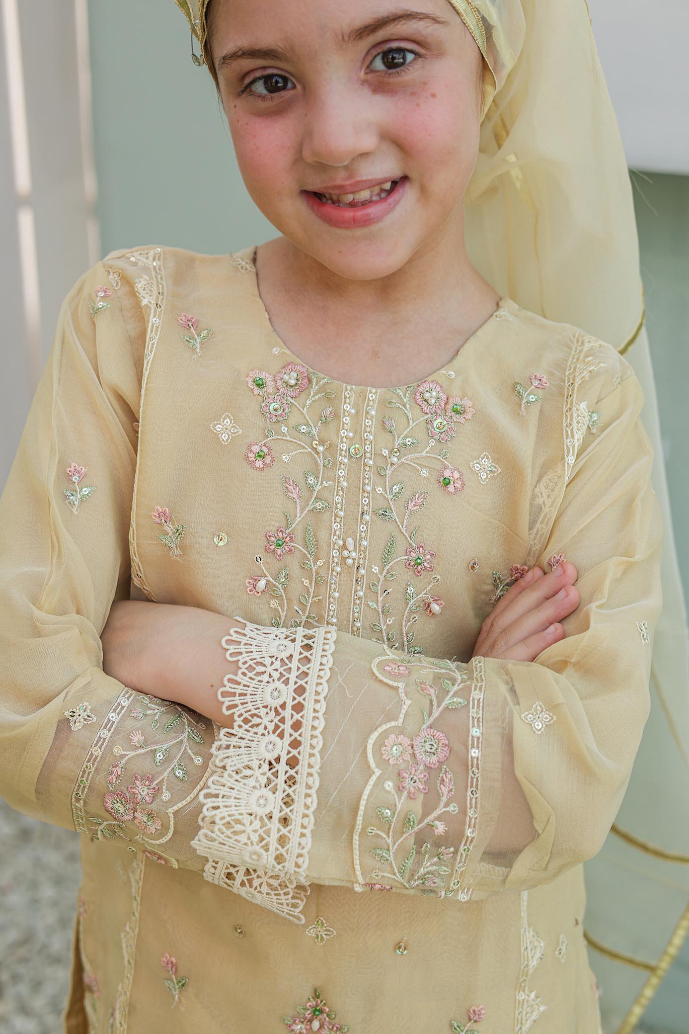 Young girl wearing a beige embroidered outfit with a matching headscarf.