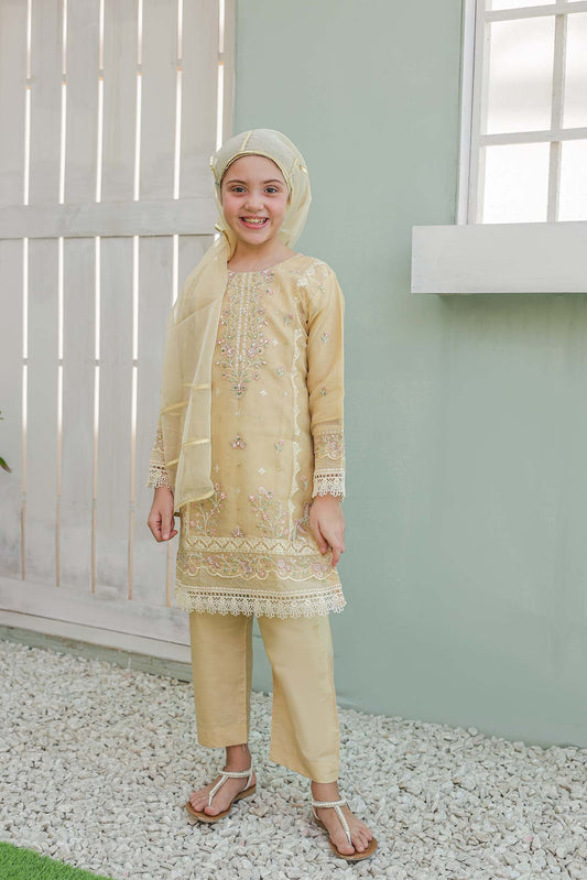 Young girl in a beige traditional outfit standing in front of a light green wall.