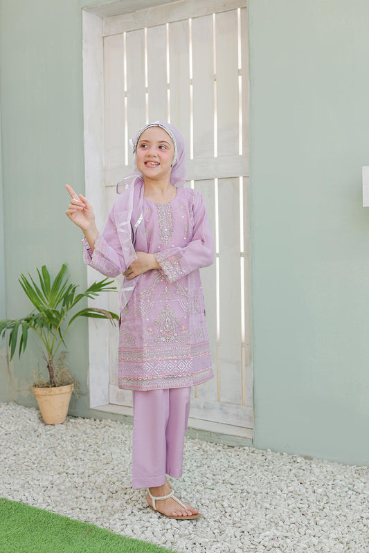 Woman in a pink traditional outfit standing in a room with a plant and white door.